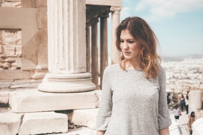 女人穿灰色长袖衬衫站在白色的混凝土柱在白天
